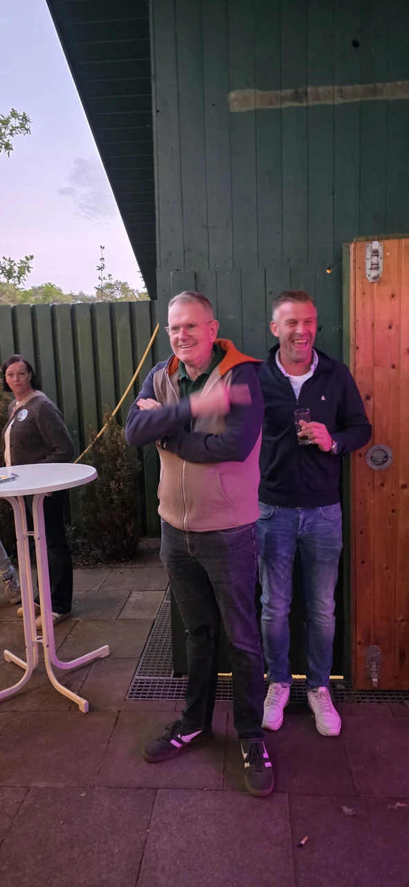 Zwei Gäste lachen am Stehtisch in der Abenddämmerung